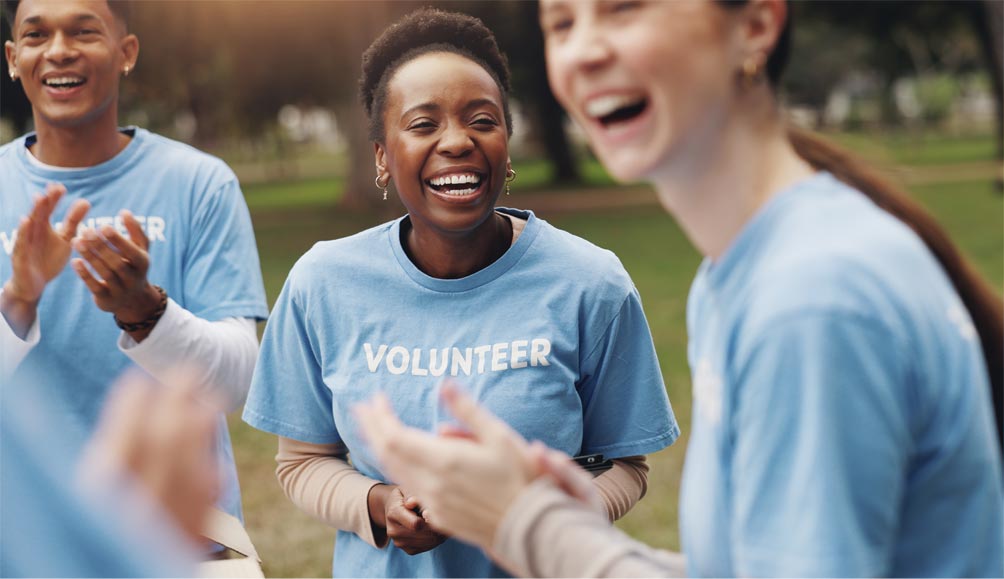 Group of volunteers from community in blue shirts clapping and interacting outdoors in a park setting