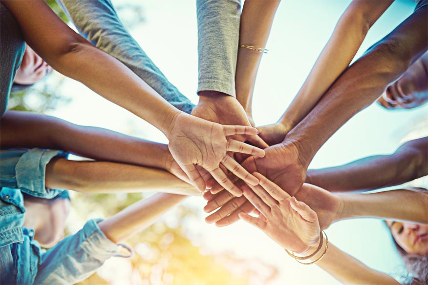 Group of people standing in a circle with hands stacked in the center symbolizing community unity