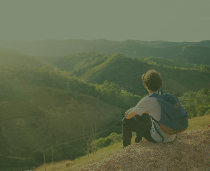 Person with blue backpack sitting on a hill overlooking other green hills