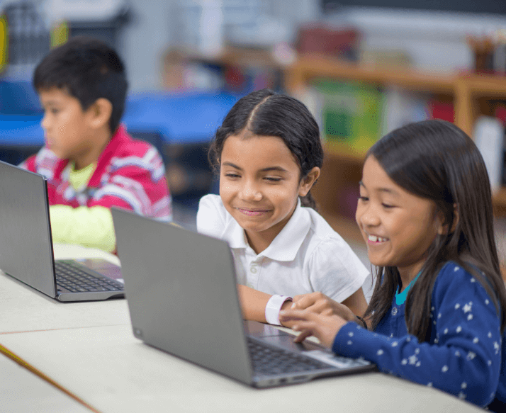 Children in a classroom using laptops for digital lessons